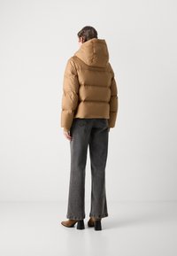 Veste en duvet marron avec une capuche, présentant un design matelassé et une coupe courte, assortie à un pantalon en jeans gris à jambes larges et des chaussures à talons marron.