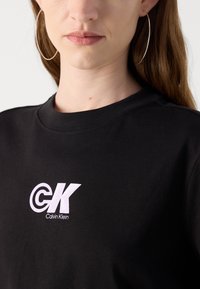 Zwarte katoenen t-shirt met een ronde halslijn, voorzien van een wit logo en de tekst "CK Calvin Klein" op de linkerkant van de borst.