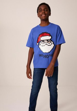 T-shirt blu con una grafica pixelata di Babbo Natale con un cappello rosso, abbinata a jeans blu scuro. Il design include il testo "HO HO HO".