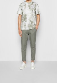 Krátký rukáv, šedé tričko s batikovaným vzorem s bílým logem, doplněné světlými zelenými tapered kalhotami a bílými teniskami. Jednoduchý, moderní design.