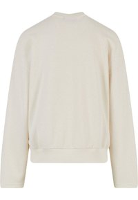 Helle beigefarbene Mesh sweatshirt mit langen Ärmeln, fallenden Schultern und einem gerippten Saum. Besitzt ein texturiertes Muster überall.