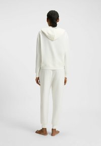 Sweatshirt à capuche blanche et pantalon de survêtement assorti en tissu doux avec des poignets côtelés. L'ensemble a une coupe décontractée et un design minimaliste.