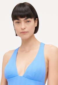 Maillot de bain bleu clair à côtes, avec un décolleté en V profond et des bretelles larges, fabriqué à partir d'un textile lisse avec une texture subtile.