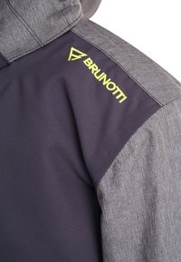 Tmavě šedá bunda se světlým šedým texturovaným ramenním dílem. Obsahuje výrazné žluté logo "BRUNOTTI" a ostré designové prvky.