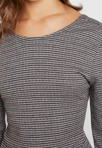 Svart- och vitrutigt mönstrat topp med rund halsringning, långa ärmar och figurnära silhuett; med ett strukturerat, stretchigt tyg.