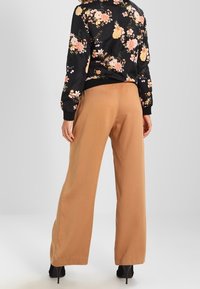 Czarna bomberka w kwiatowy wzór z długimi rękawami, zestawiona z jasnobrązowymi, szerokimi spodniami. Oba elementy mają gładkie tekstury i casualowy design.