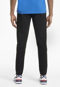 Zwarte taps toelopende sportbroeken met zijpanelen en naaddetailing, gecombineerd met meerkleurige sportschoenen met een witte zool en branding.