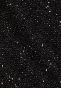 Tessuto nero testurizzato con un motivo intrecciato, arricchito da piccole paillettes che riflettono la luce, creando un effetto scintillante.