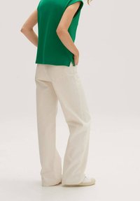 Zelený krátký rukáv top, který je spojen s volně padnoucími krémovými širokými kalhotami, s hladkou texturou a jemnými stehovými detaily.