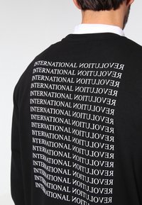 Felpa nera con un audace motivo testuale ripetuto in bianco sul retro con la scritta "INTERNATIONAL REVOLUTION". Maniche lunghe e girocollo.