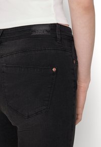 Svarta denimjeans med slim fit, med en logotypapplikation vid midjan, diskreta nitar och klassisk femficksdesign.