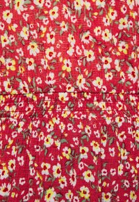 Rød stof med et blomstermønster i gule og hvide blomster. Rynket tekstur ved taljen med folder, der skaber et svævende udseende.