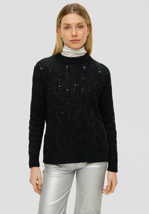 Czarny dzianinowy sweter z teksturowanym splotem warkoczowym, z żeberkowym kołnierzem i mankietami. Nosi się go na jasnym golfie.