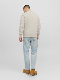 Beige sweatshirt met lange mouwen, ronde hals en geribbelde manchetten, gecombineerd met lichtblauwe spijkerbroeken en beige instappers.