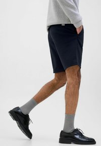 Pantalones cortos azul marino con una textura suave, que cuentan con bolsillos laterales. Combinados con calcetines grises de canalé y zapatos de cuero negro con detalles brogue.