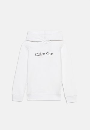 Fehér kapucnis pulóver hosszú ujjakkal és fekete Calvin Klein logóval a mellkas közepén, egyszínű háttér előtt.