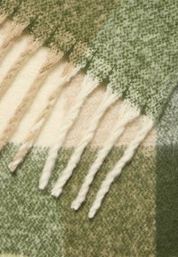 Coperta a motivo a quadri tessuta in tonalità di verde, crema e beige, con bordi frangiati, realizzata in morbido tessuto di lana testurizzata.