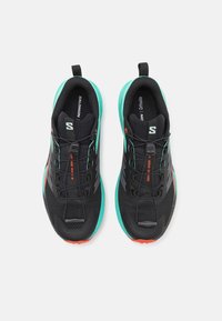 Scarpe da ginnastica nere con tomaia in mesh, dettagli turchesi e suola testurizzata. Presentano un sistema di allacciatura sicuro e dettagli di branding.
