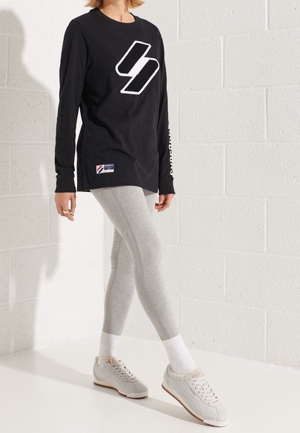 Maglietta nera a maniche lunghe con logo bianco, leggings grigi e sneakers chiare. Tessuto morbido; vestibilità comoda; stile minimalista.