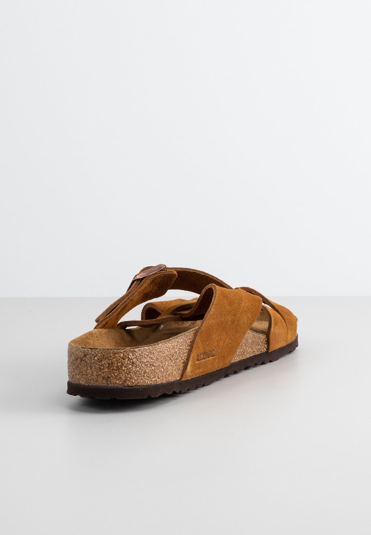 Sandales en suède marron avec une semelle en liège, dotées de brides croisées et d'une semelle intérieure texturée, conçues pour le confort et un usage décontracté.