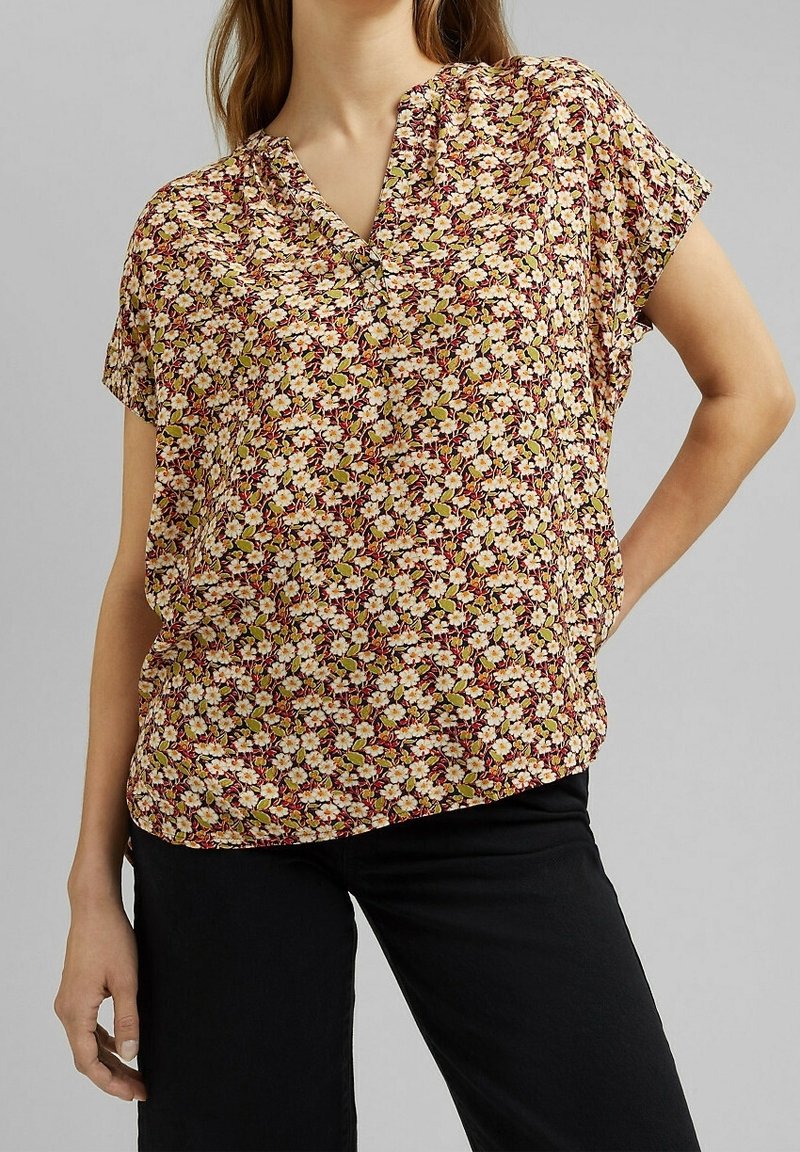 Blusa con motivo floreale, scollatura a V, maniche corte e vestibilità comoda. Presenta fiori rosa, bianchi e verdi su uno sfondo bordeaux.