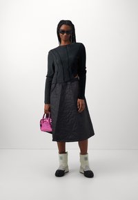 Zwarte cropped trui met textuurdetails, gecombineerd met een knielange gewatteerde zwarte rok. Wit en zwarte laarzen, en een kleine glanzende roze handtas.