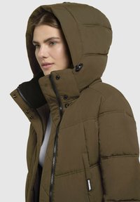 Braune Daunenjacke mit Kapuze, mit einem Reißverschluss, Druckknöpfen und Taschen an den Seiten. Das Material hat eine glatte Textur und ein gestepptes Design.