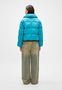 Tirkizna puffer jakna s krojenjem iznad struka i širokim ovratnikom, uparena s trapericama visokog struka i širokih nogavica u izbleđenoj nijansi. Glatka tekstura.