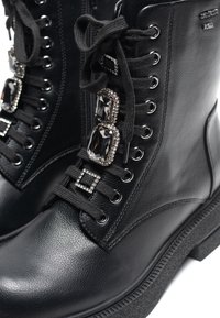 Black leather ankle boots with lace-up design. Features decorative gems and metallic hardware on the sides. Textured sole adds grip.