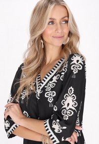 Blusa nera con motivi floreali e geometrici bianchi, con scollatura a V e rifiniture a strisce sulle maniche. Tessuto leggero e morbido.