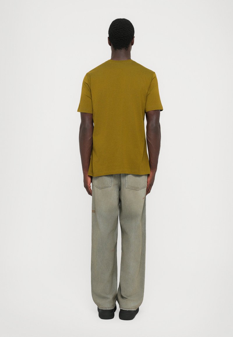 Olivgrön kortärmad skjorta kombinerad med ljusgrå baggy jeans. Outfiten har en avslappnad passform och en enkel design utan utsmyckningar.