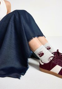Denim maxiskørt i mørkeblå med en flosset kant, parret med maroon ruskind sneakers og grå ribbede sokker med logo detaljer.