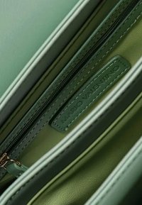 Sac en cuir vert avec un compartiment zippé, texture lisse et une étiquette portant l'inscription "Mario Valentino". L'intérieur présente une doublure d'un vert plus clair.