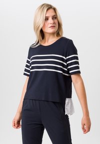 Marineblauwe T-shirt met witte strepen; korte mouwen en ronde halslijn. Bevat een gestructureerde witte kantzoom die onder het shirt uitsteekt.
