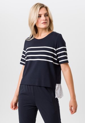 Marineblauwe T-shirt met witte strepen; korte mouwen en ronde halslijn. Bevat een gestructureerde witte kantzoom die onder het shirt uitsteekt.