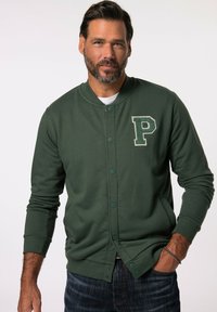 Felpa verde, leggera, con collo rotondo e chiusura a bottoni, caratterizzata da una toppa testurizzata con una "P" sulla sinistra. Polsini e orlo a coste.