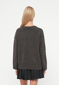 Mörkgrå, stickad tröja med rund halsringning, långa ärmar och ribbat avslut. Baksidan är enkel utan dekorationer eller mönster.