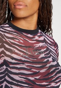 Nærbillede af en person iført en lyserød og sort tigerstribet top med teksten "Juicy Couture" og rhinstenpynt på brystet.