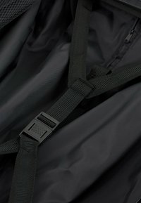 Interior de nylon negro con correas ajustables negras y hebilla de plástico. Textura suave con un brillo sutil, que cuenta con un compartimento con cremallera.