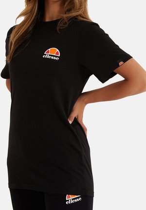 Mujer con camiseta y leggins negros de Ellesse, con los logotipos visibles en el pecho, la manga y el muslo.