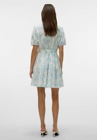 Abito a maniche corte in tessuto leggero con motivo floreale blu, aderente in vita, svasato, sopra il ginocchio, abbinato a scarpe con tacco basso.