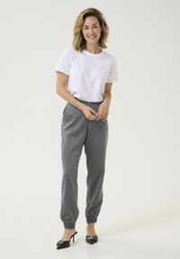 T-shirt blanc, pantalon gris fuselé avec des poignets élastiques et chaussures à talons noires. Tenue décontractée aux lignes simples et minimalistes.