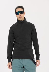 Schwarzer Quarter-Zip-Pullover mit langen Ärmeln, aus strukturiertem Stoff, mit Raglan-Nähten. Getragen mit hellblauen Cargo-Shorts.