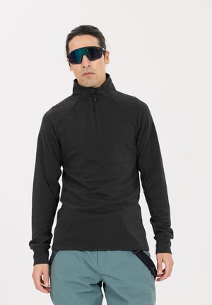 Schwarzer Quarter-Zip-Pullover mit langen Ärmeln, aus strukturiertem Stoff, mit Raglan-Nähten. Getragen mit hellblauen Cargo-Shorts.