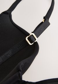 Must rinnahoidja rihm kuldse reguleeritava klambriga ja reljeefse brändinguga elastsel paelal neutraalsel taustal.