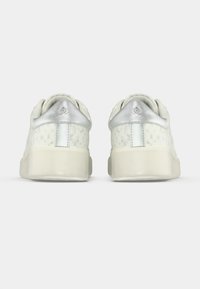 Paire de baskets blanches vues de dos, avec des accents argentés au talon et un motif texturé subtil sur les côtés.