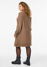 Bruine gebreide sweaterjurk met lange mouwen en zijsplitsingen. Draag het met zwarte enkellaarsjes. Zachte textuur en relaxte pasvorm.