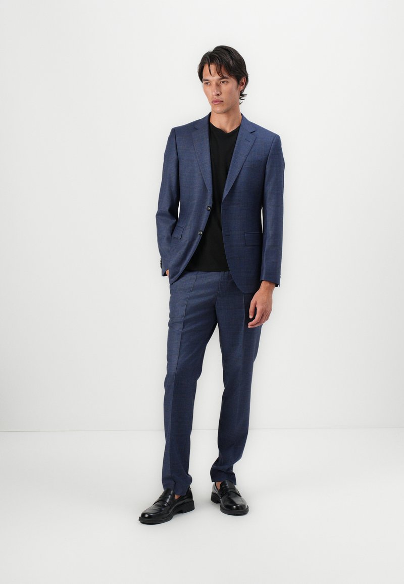 Traje de patrón a cuadros en azul, hecho de tejido liviano. Pantalones a juego, diseño ajustado, y combinado con una camiseta negra y zapatos negros.