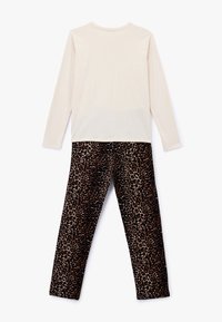 Crèmekleurige top met lange mouwen, gecombineerd met zwarte en bruine broek met luipaardprint, met een zachte textuur en een ontspannen pasvorm.