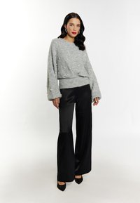 Pulover gri texturat cu accesorii, asortat cu pantaloni din satin negri, cu picioare largi. Pantofii negri cu vârf ascuțit completează look-ul.